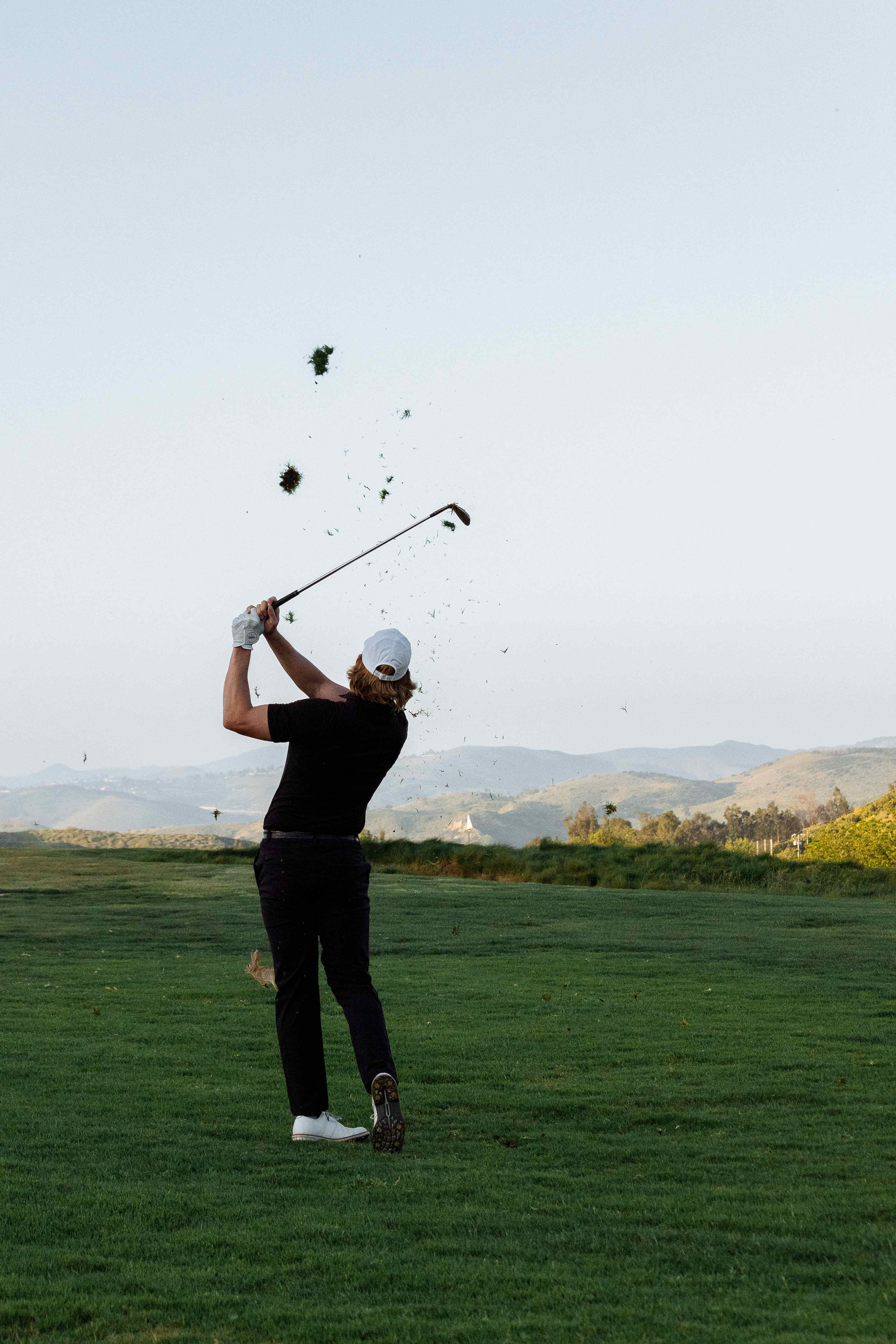 Golfer holding a strong finish after a full swing on the course, divot flying
