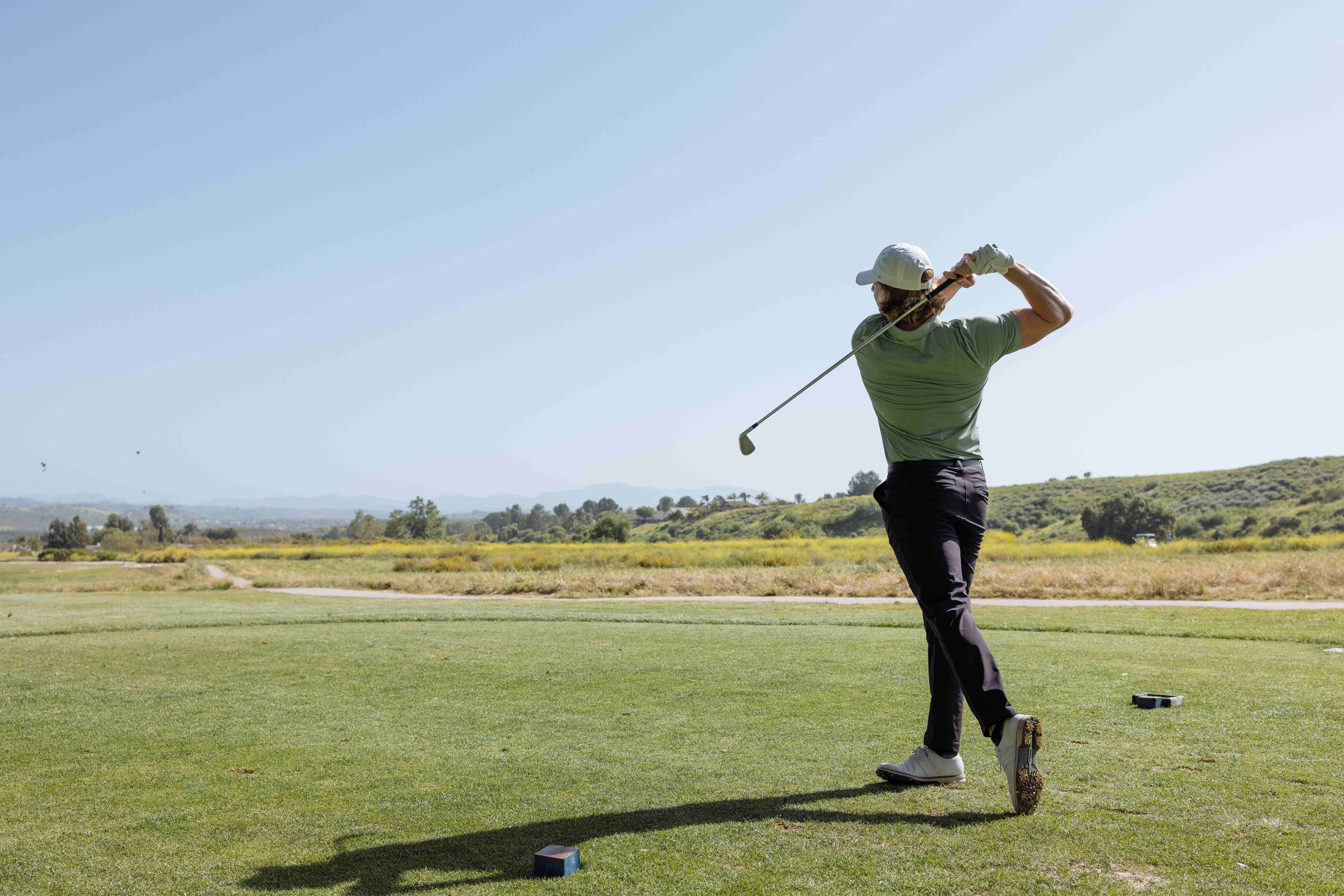 Golfer holding his finish after a swing, looking out over an open course