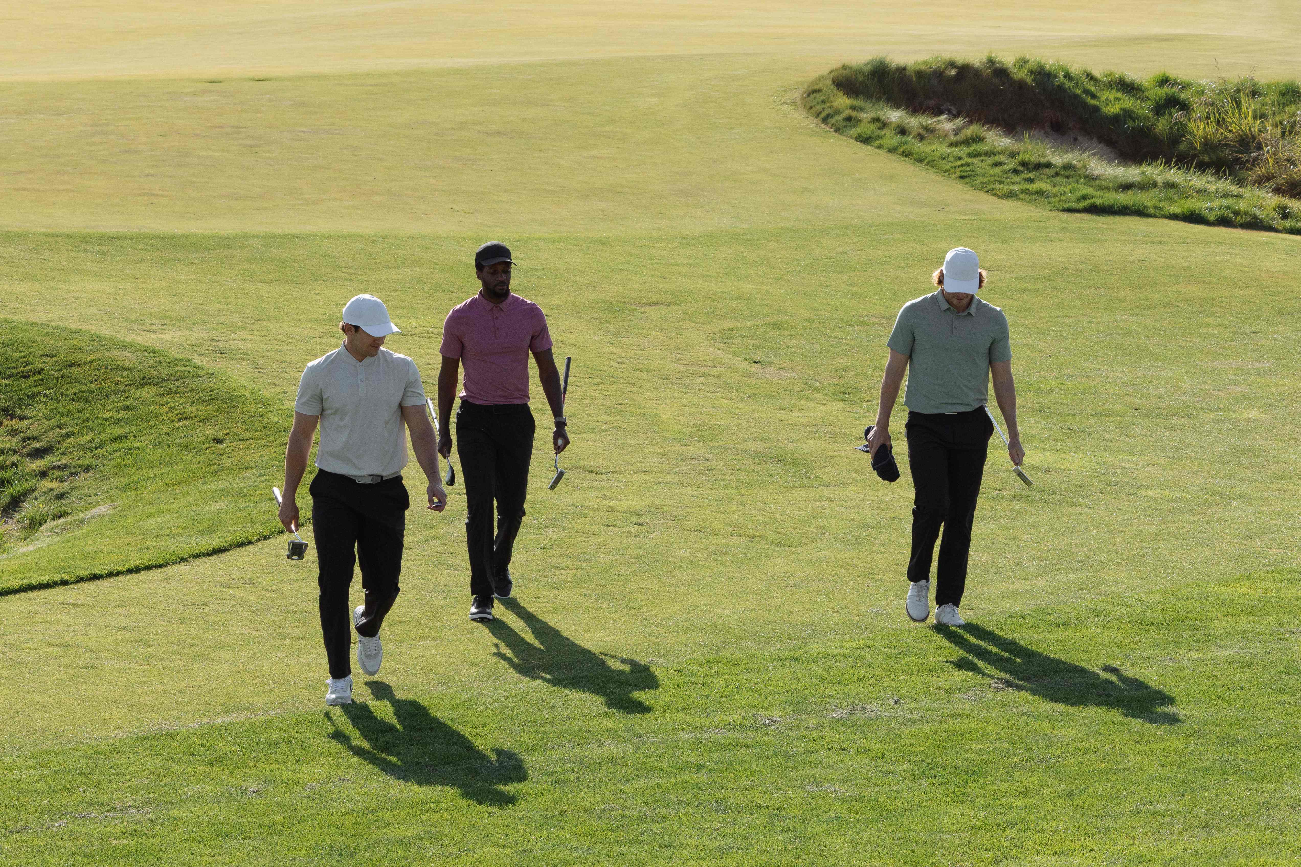 Three golfers walking down a sunlit fairway together carrying their clubs on a relaxed round